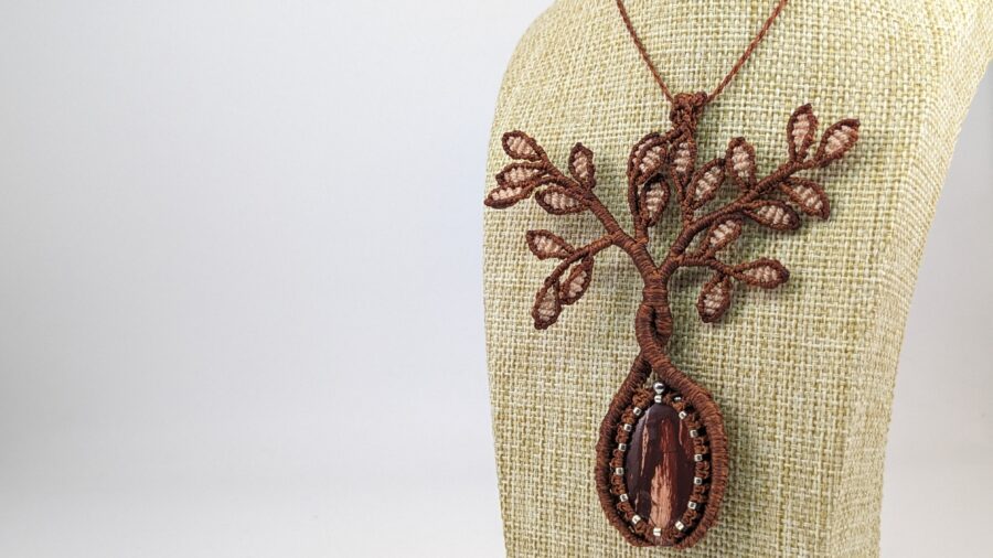 Photo d'un bijou en macramé ocre sur buste, en forme d'arbre et pourvu d'une pierre en jaspe rouge